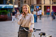 © Cavan Images - A smiling woman with a bicycle enjoys a sunny day in a bustling city