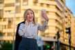 © Cavan Images - Young woman taking a selfie on a city street during sunset
