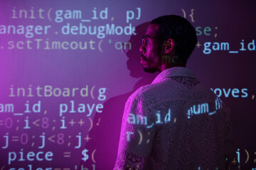 side view of a person standing in a dimly lit room while observing computer code projected on a wall