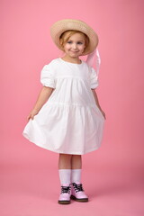 little cute girl in white summer dress in hat and shoes, knee socks posing in studio on pink backgro