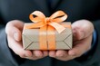 © Katawut - A person holds a beautifully wrapped gift box with an orange ribbon, symbolizing generosity and celebration.