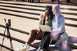 © Johnér - Happy multiracial friends vlogging through smart phone while sitting on steps at street