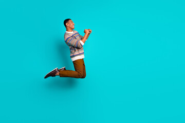 Wall Mural - Full size photo of nice young man raise fists jump empty space wear sweater isolated on teal color background