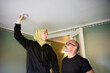 © Johnér - Shaved head man with woman in hijab installing smoke detector on ceiling at home