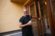 © Johnér - Portrait of smiling mature man carrying ladder and holding smoke detector while opening door of building