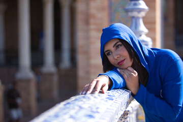 Portrait of Moroccan woman, young, beautiful, brunette, with blue abaya, with hood on, with sweet and dreamy look leaning on a beautiful tiled railing. Concept ethnicity, diversity, femininity, beauty