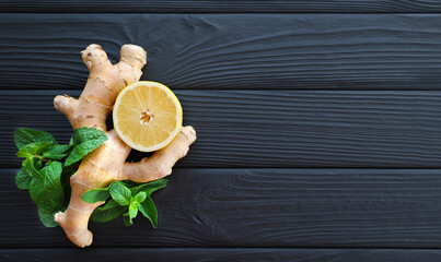 Ginger root, lemon, and fresh mint on a black wooden surface. A fresh lemon slice, ginger root, and sprigs of vibrant mint arranged on a dark wooden surface. Top view. Free space for text.