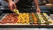 © BerkahStock - A chef garnishes a colorful platter of assorted appetizers in a restaurant kitchen.