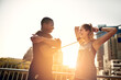 © peopleimages.com - Runner, man and woman with warm up on bridge with exercise, laugh and funny joke at sunrise in city. People, couple and stretching arms in street with lens flare, fitness and workout in morning