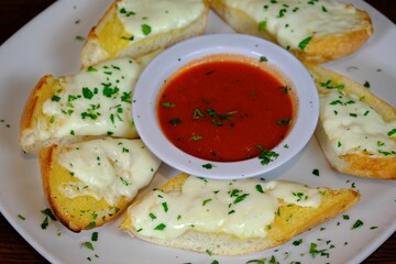 garlic bread pieces topped with melted cheese and served with tomato sauce on a white plate