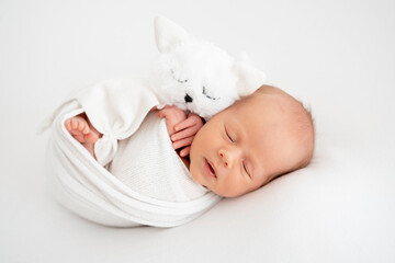 a newborn baby is lying in a diaper on a bed on a white isolated background, a place for text, a small baby boy is sleeping sweetly with a soft toy, a close-up portrait