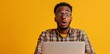 © Stanley - Young man with glasses expresses surprise while working on a laptop against a vibrant yellow background