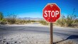 © Suphawan - Weathered stop sign at a desert intersection, surrounded by sand and sparse vegetation, under a clear blue sky.
