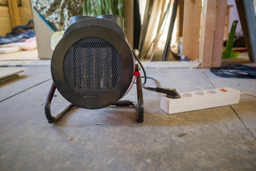 an electric heat gun on the floor connected to an extension cord outlet in a frame house under construction