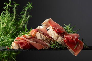 Poster - Ciabatta with prosciutto and rosemary on a black background.