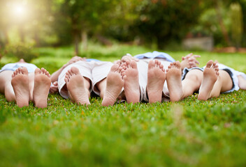 Family, grass and feet of parents and children in backyard for bonding, relaxing and fun together outdoors. Morning, nature and toes of mom, dad and kids on field for holiday, vacation and weekend