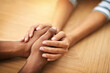 © peopleimages.com - People, holding hands and care with sympathy for support, trust or understanding on wooden table. Closeup, interracial or touch with empathy for listening, grief or loss in hope or faith together