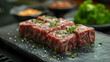 © KaiTong - Close-up of raw marbled beef steak cubes garnished with chopped chives, ready for grilling or cooking on a dark slate surface