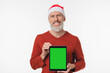 © InsideCreativeHouse - Happy mature middle-aged man in red Santa Claus hat holding digital tablet showing green screen for mockup copy space isolated on white background. New Year Merry Christmas winter holidays concept