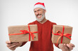 © InsideCreativeHouse - Happy mature middle-aged man in red Santa Claus hat holding in camera Christmas New Year presents gifts isolated in white background. New Year Merry Christmas winter holidays concept