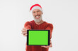 © InsideCreativeHouse - Happy mature middle-aged man in red Santa Claus hat holding digital tablet showing green screen for mockup copy space isolated on white background