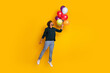 © deagreez - Young man in black shirt with colorful balloons jumping on yellow background, expressing joy and excitement