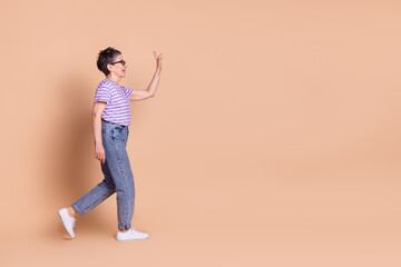 Photo of adorable lovely nice retired woman wear striped trendy clothes walk look empty space isolated on beige color background