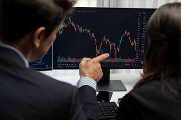 Two business traders discussing on dynamic stock market in currency rate investment trading on two pc screens with compare real time graph on risk or profit point of data at modern office. Postulate.