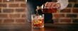 © Daylife - A bartender pours amber liquid over ice into a glass, creating a classic cocktail against a rustic brick backdrop.