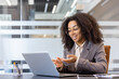 © Tetiana - Smiling young African American woman sitting in office at desk in front of laptop and talking online on video call gesturing with hands