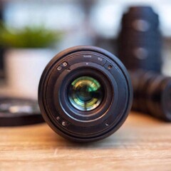 A close-up of a high-resolution digital camera lens in sharp focus, capturing the inner mechanics, with the blurred background showcasing various photography equipment.