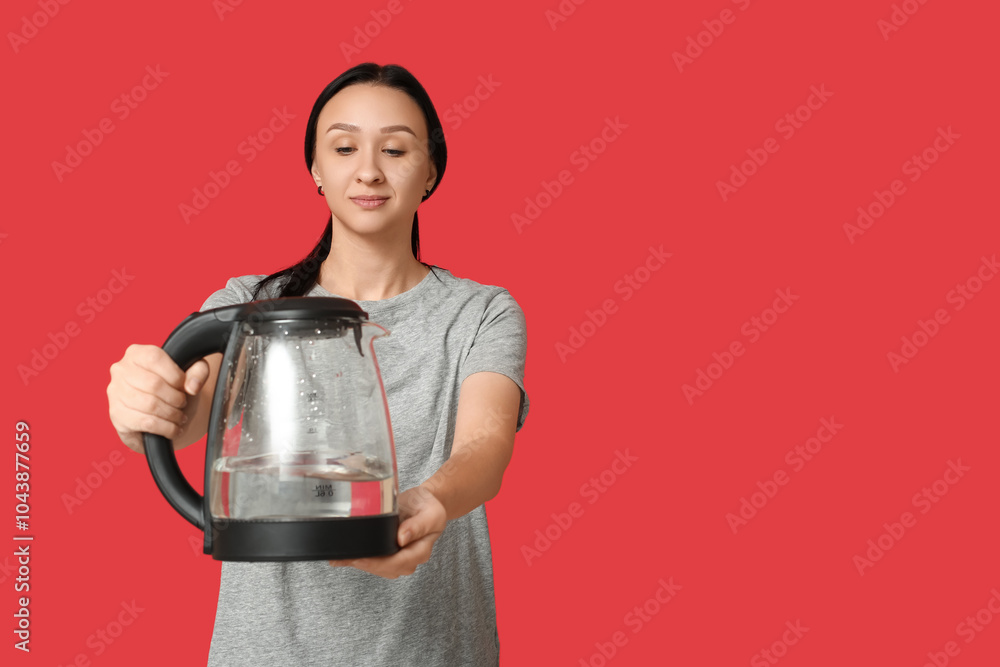 Beautiful young woman with modern electric kettle on red background