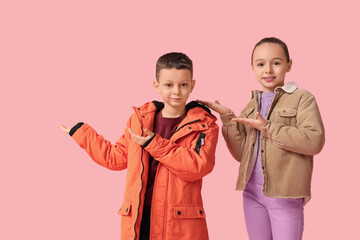 Canvas Print - Cute little happy children in warm winter clothes pointing at something on pink background