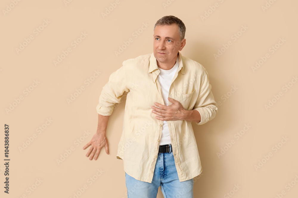 Mature man suffering from chest pain on beige background