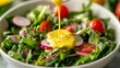 © thenort - Close-up of a fresh green salad with cherry tomatoes, radishes, and a honey mustard dressing being poured over the top.