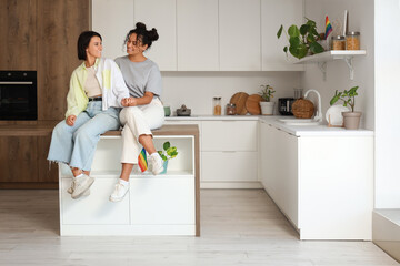 Wall Mural - Young lesbian couple sitting on table in kitchen