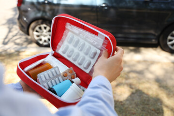 Woman holding open first aid kit near car outdoors