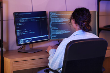 Wall Mural - young african-american qa engineer working with computer in office at night, back view