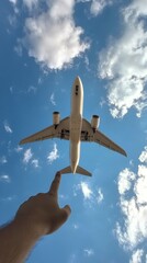 A person reaching towards a plane flying high in a clear blue sky on a sunny day