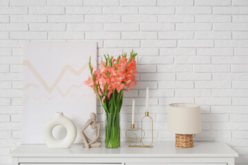 Wall Mural - Vase with gladiolus flowers, lamp and decor on commode near white brick wall