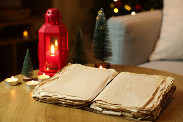 Opened old book, glowing lantern and candles on table in dark room, closeup. Christmas story concept