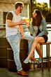 © peopleimages.com - Toast, drinks and happy couple laughing at rooftop party, holiday and new year celebration together. Smile, man and woman cheers with alcohol cocktails for funny conversation, love and outdoor date