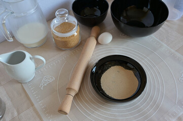 Baking ingredients for baking sweet buns, yeast in black bowl dishes with rolling pin on a table