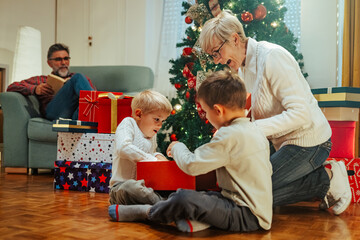 Wall Mural - Excited children opening christmas presents by the tree with family