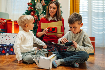 Wall Mural - Two little brothers unpacking christmas presents with their mother