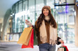 © Home-stock - Happy European woman holding shopper bags and smiling, standing on city street after successful Christmas shopping in mall. Winter sale concept