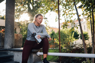 Wall Mural - Young sportswoman taking break outdoors holding water bottle