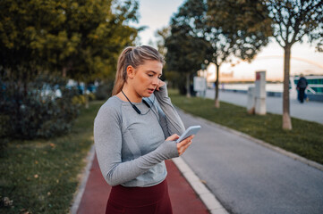 Wall Mural - Young sporty woman using smartphone after running in the city park