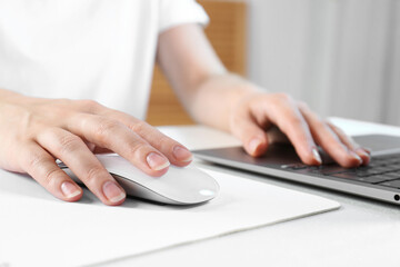 Sticker - Woman using computer mouse while working with laptop at white table, closeup