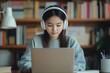 © Anton - Focused girl with headphones using laptop at library desk